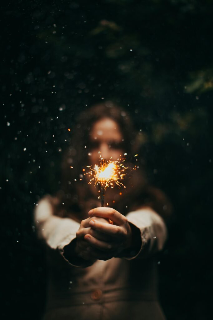 A young woman holds a sparkler outdoors at night, creating a magical and festive atmosphere.