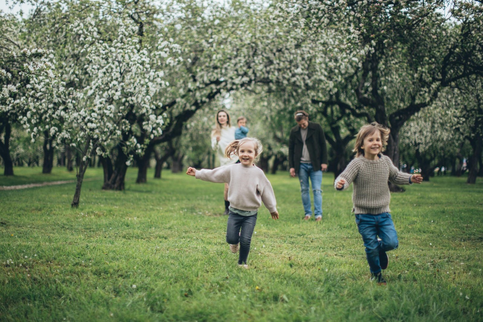 A happy family running and playing among blooming trees in a lush green park during spring.
